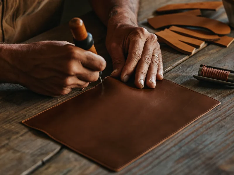 Mains piquant du cuir sur un établi avec alêne et fil ciré
